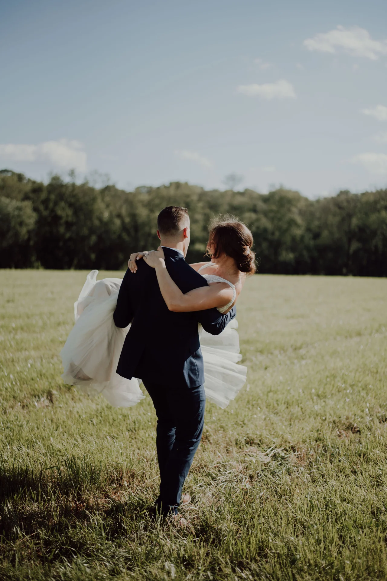 Un marié porte sa femme dans un champ — photographie de Katelyn MacMillan
