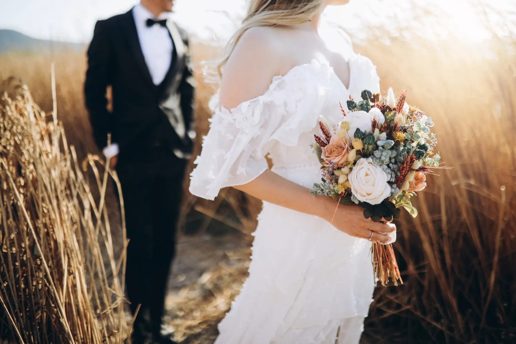 Bride holding her bouquet in a field at sunset